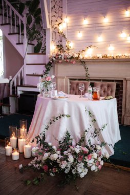 Restoranın ziyafet salonundaki yeni evlilerin başkanlığı mumlar ve yeşil bitkilerle süslenmiş, salkımlar tavandan sarkmış.