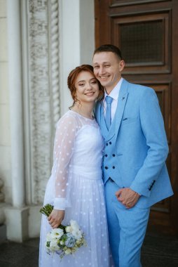 bride in a light wedding dress with a bouquet next to the groom in a blue suit