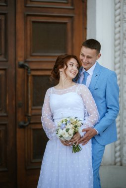 bride in a light wedding dress with a bouquet next to the groom in a blue suit