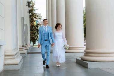 bride in a light wedding dress with a bouquet next to the groom in a blue suit