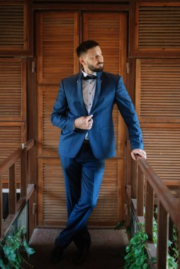 portrait of a groom with a beard in a blue suit and bow tie