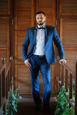 portrait of a groom with a beard in a blue suit and bow tie