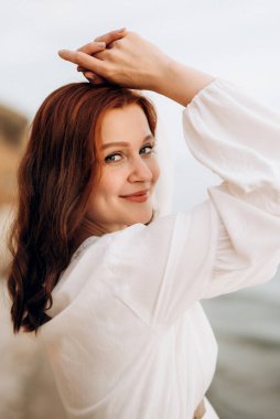 Sahil kenarında beyaz elbiseli, kahverengi saçlı hamile bir kız.