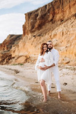 Deniz kıyısında, kil kayalıkların yanında beyaz elbiseli bir kızla bir adam.