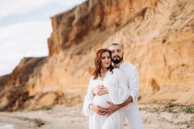 Deniz kıyısında, kil kayalıkların yanında beyaz elbiseli bir kızla bir adam.