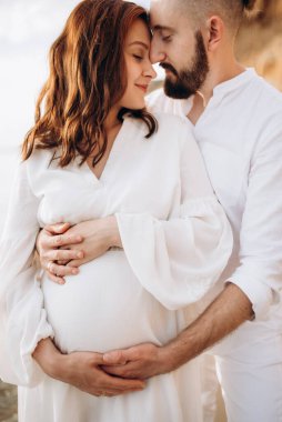 Deniz kıyısında, kil kayalıkların yanında beyaz elbiseli bir kızla bir adam.