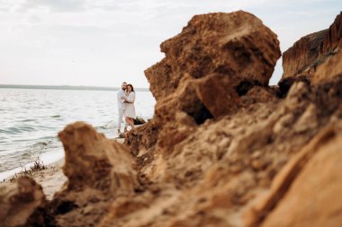 Deniz kıyısında, kil kayalıkların yanında beyaz elbiseli bir kızla bir adam.
