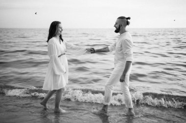 Deniz kıyısında, kil kayalıkların yanında beyaz elbiseli bir kızla bir adam.