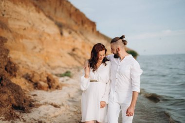 Deniz kıyısında, kil kayalıkların yanında beyaz elbiseli bir kızla bir adam.