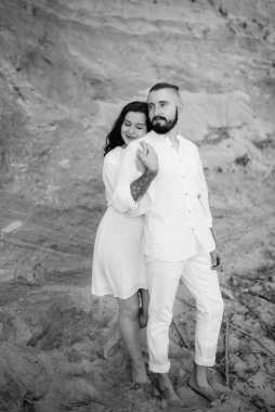 Deniz kıyısında, kil kayalıkların yanında beyaz elbiseli bir kızla bir adam.