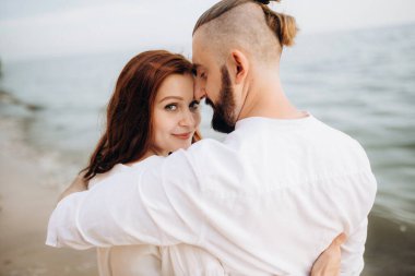 Deniz kıyısında, kil kayalıkların yanında beyaz elbiseli bir kızla bir adam.