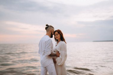 Deniz kıyısında, kil kayalıkların yanında beyaz elbiseli bir kızla bir adam.