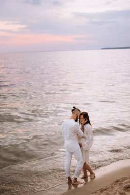 Deniz kıyısında, kil kayalıkların yanında beyaz elbiseli bir kızla bir adam.