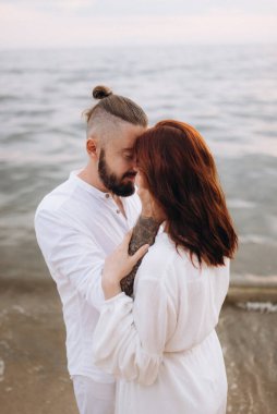 Deniz kıyısında, kil kayalıkların yanında beyaz elbiseli bir kızla bir adam.