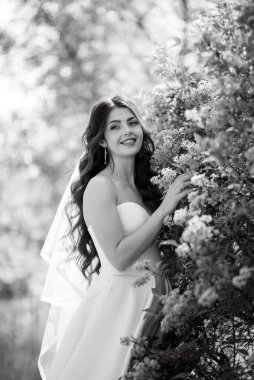 young girl bride in a white dress in a spring forest in lilac bushes on a wedding day