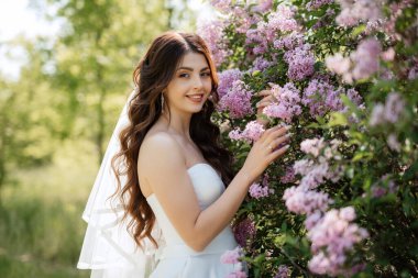 young girl bride in a white dress in a spring forest in lilac bushes on a wedding day