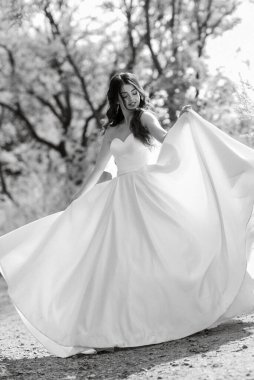 a young girl bride in a white dress is spinning on a path in a spring forest on a wedding day