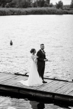 the first meeting of the bride and groom in wedding dresses on the pier near the water