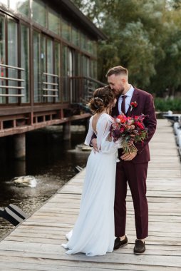 the first meeting of the bride and groom in wedding dresses on the pier near the water