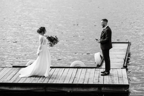 the first meeting of the bride and groom in wedding dresses on the pier near the water