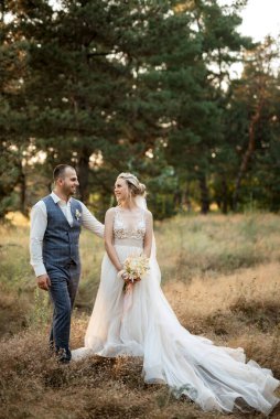 the groom and the bride are walking in the forest on a bright day