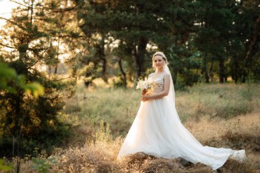 bride blonde girl with a bouquet in the forest in the sunset light