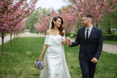 newlyweds walk in the park on the grass among cherry blossoms