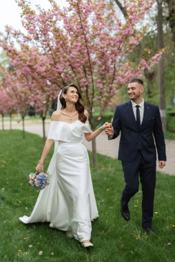 newlyweds walk in the park on the grass among cherry blossoms