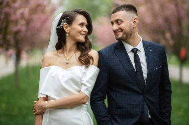 newlyweds walk in the park on the grass among cherry blossoms