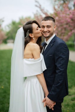 newlyweds walk in the park on the grass among cherry blossoms