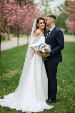 newlyweds walk in the park on the grass among cherry blossoms