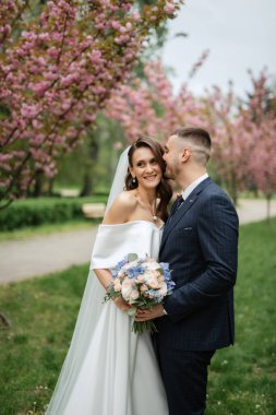 newlyweds walk in the park on the grass among cherry blossoms
