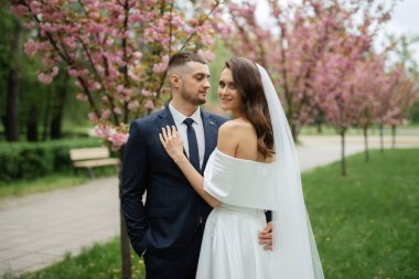 newlyweds walk in the park on the grass among cherry blossoms