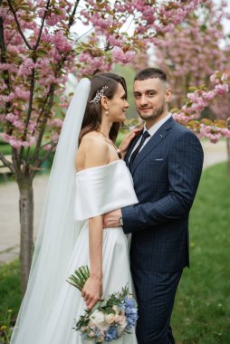 newlyweds walk in the park on the grass among cherry blossoms