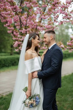 newlyweds walk in the park on the grass among cherry blossoms