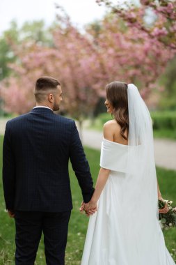 newlyweds walk in the park on the grass among cherry blossoms