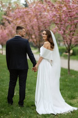 newlyweds walk in the park on the grass among cherry blossoms