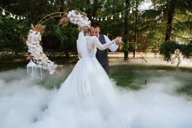 the first wedding dance of the bride and groom on a green meadow near the wedding arch