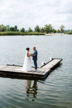 the first meeting of the bride and groom in wedding dresses on the pier near the water