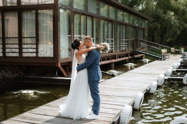 the first meeting of the bride and groom in wedding dresses on the pier near the water