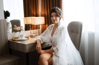 bride in a veil with makeup drinks morning coffee in a hotel