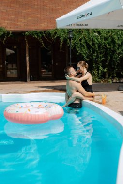 Mayolu bir erkek ve bir kız dinleniyor, güneşleniyor ve mavi havuzun yanında eğleniyorlar.