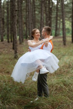 Beyaz kısa elbiseli genç çift ve ağaçların arasında, çam ormanında gri takım elbiseli damat.