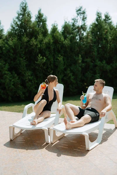 水着姿の男と女はリラックスして日光浴を楽しんでる青いプールの近くで — ストック写真