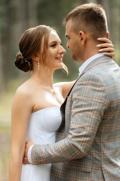 stock image young couple bride in a white short dress and groom in a gray suit in a pine forest among the trees