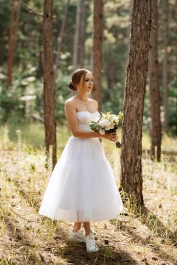 Ağaçların arasında, bahar çam ormanında beyaz kısa elbiseli genç gelin.