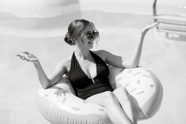 a girl in a black swimsuit floats on an inflatable circle in a blue pool