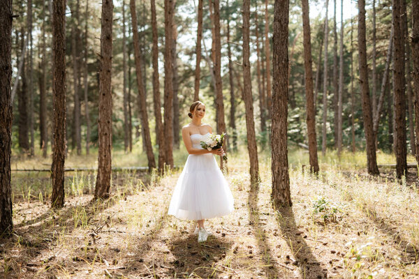 Young bride in a white short dress in a spring pine forest among the trees