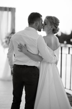 Gelin ve damat, nehrin kıyısındaki bir iskelede sarı bir günbatımının arkaplanına karşı.