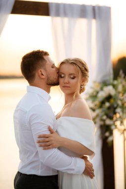 bride and groom against the backdrop of a yellow sunset on a pier near the river